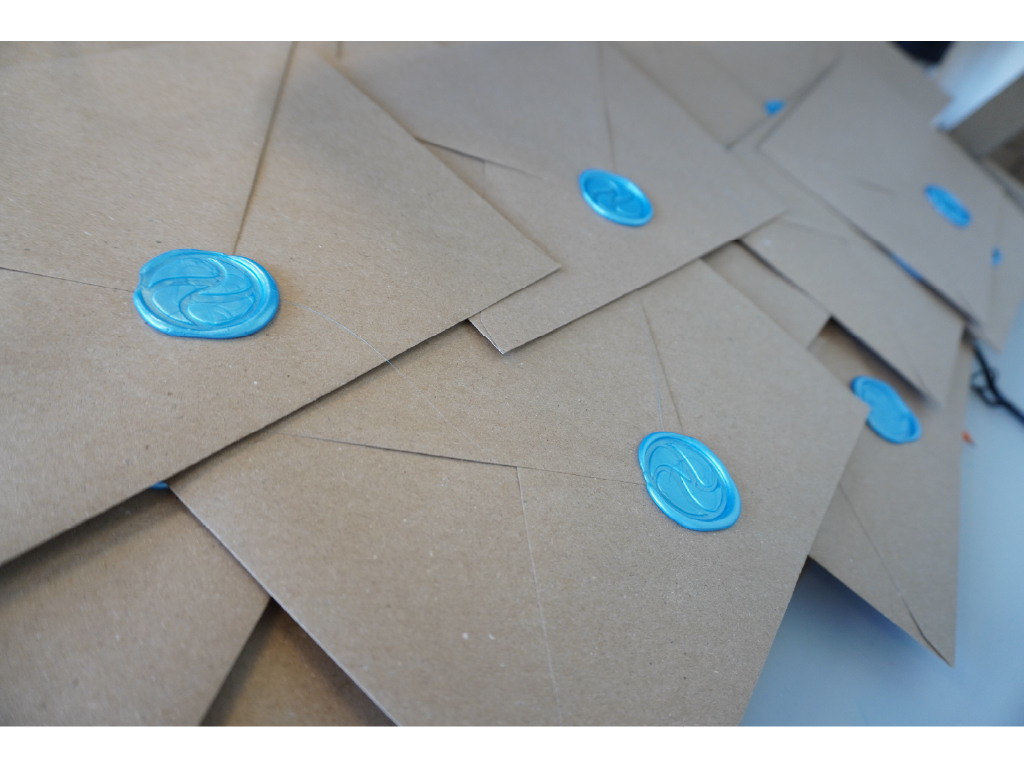 A stack of kraft invitation envelopes, each closed with a blue wax LA Micro seal